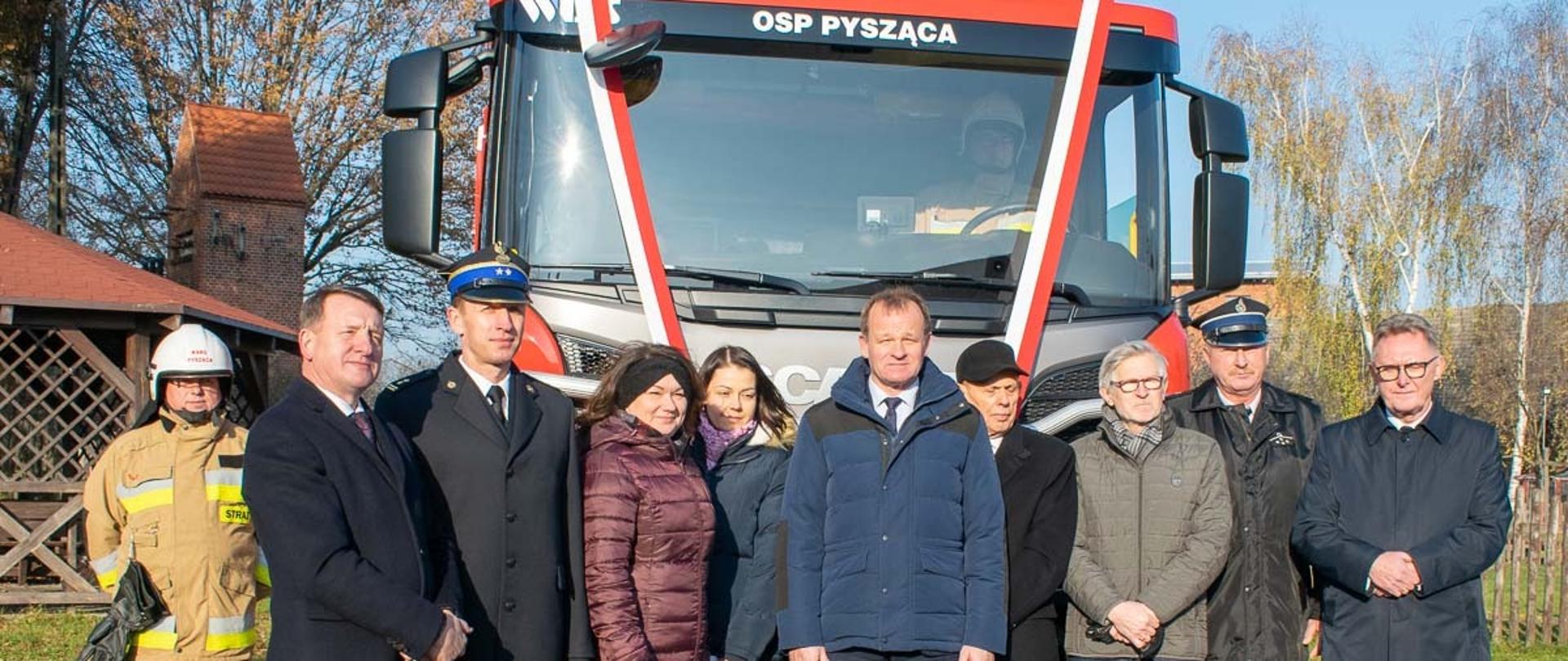Zdjęcie wykonane podczas uroczystości wprowadzenia nowego samochodu ratowniczo-gaśniczego do podziału OSP Pysząca. Na zdjęciu znajdują się parlamentarzyści zastępca Wielkopolskiego Komendanta Wojewódzkiego, przedstawiciele samorządu terytorialnego oraz zaproszeni gości i druhowie. 