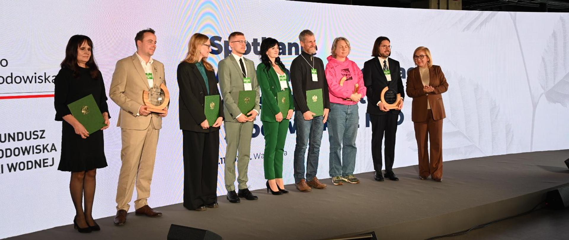 Zdjęcie przestawia dziewięć osób stojących w jednym rzędzie i pozujących do zdjęcia. Od lewej ośmiu laureatów konkursu Klimatyczny Człowiek Roku i obok ministra Klimatu i Środowiska Paulina Hennig-Kloska, która przed chwilą wręczała im nagrody. 