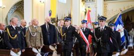 Poczet sztandarowy strażaków podczas wejścia do kościoła zmierza w stronę ołtarza na tle strażaków i gości podczas mszy