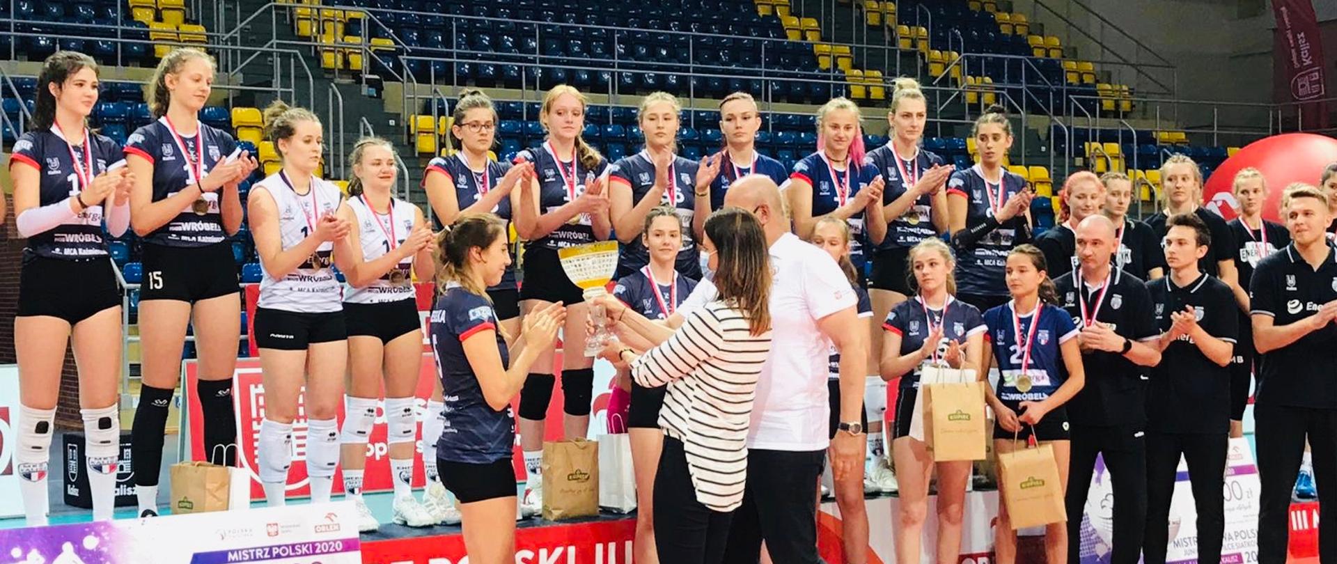 Minister Sportu Danuta Dmowska-Andrzejuk ze sportowym pucharem. Sportowcy biją brawo.