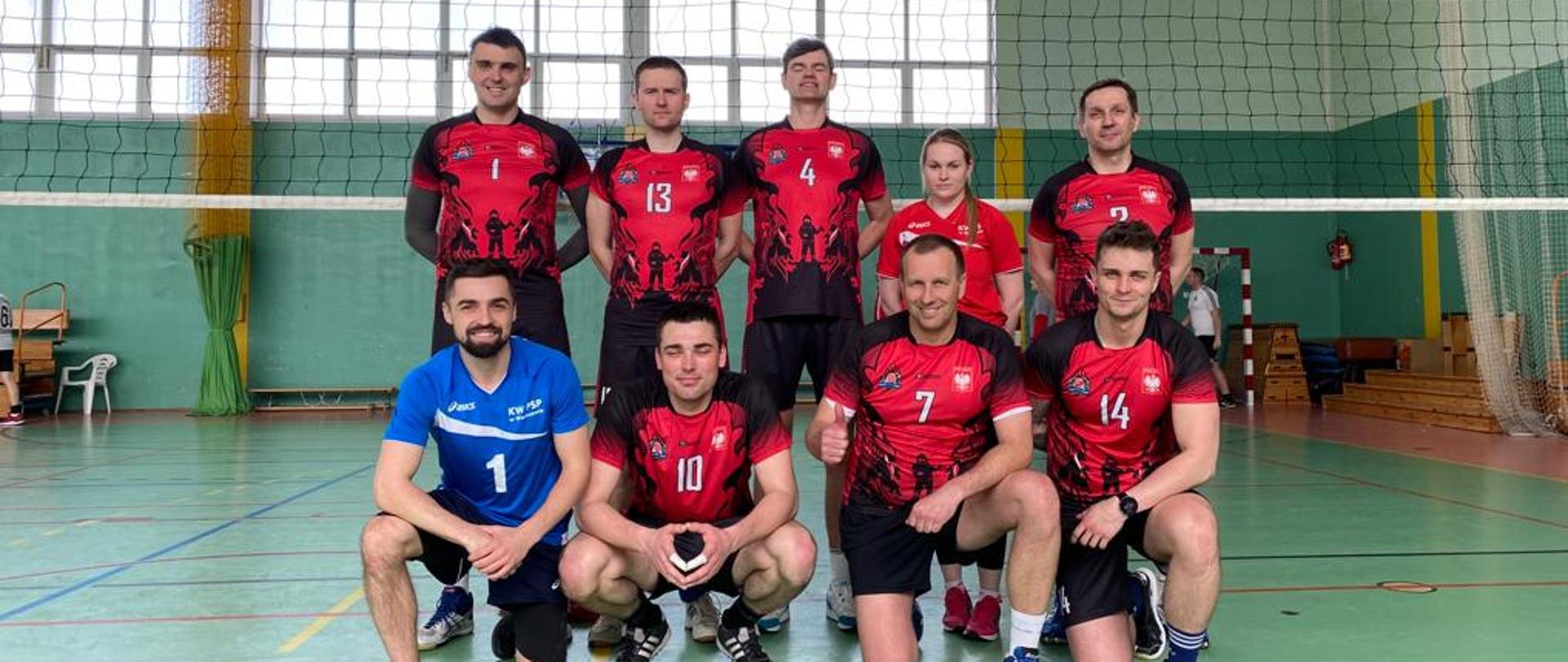 zwycięska drużyna zawodów - drużyna Komendy Wojewódzkiej PSP w Warszawie. Pierwszy rząd - 4 kucające osoby, drugi rząd - 5 stojących osób. Wszyscy oprócz jednej osoby ubrani w czerwono czarne koszulki i czarne spodenki.