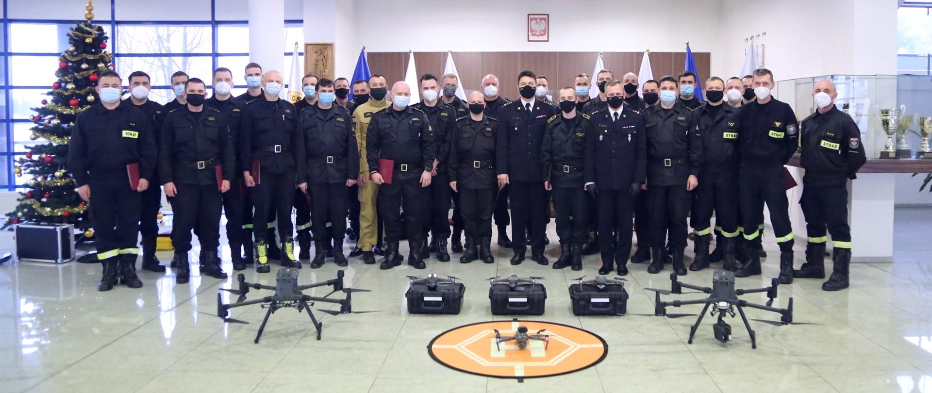 Grupowe zdjęcie Komendanta Centralnej Szkoły PSP wraz z Zastępcą oraz instruktorami w otoczeniu kursantów. Przed nimi sprzęt wykorzystywany na szkoleniu