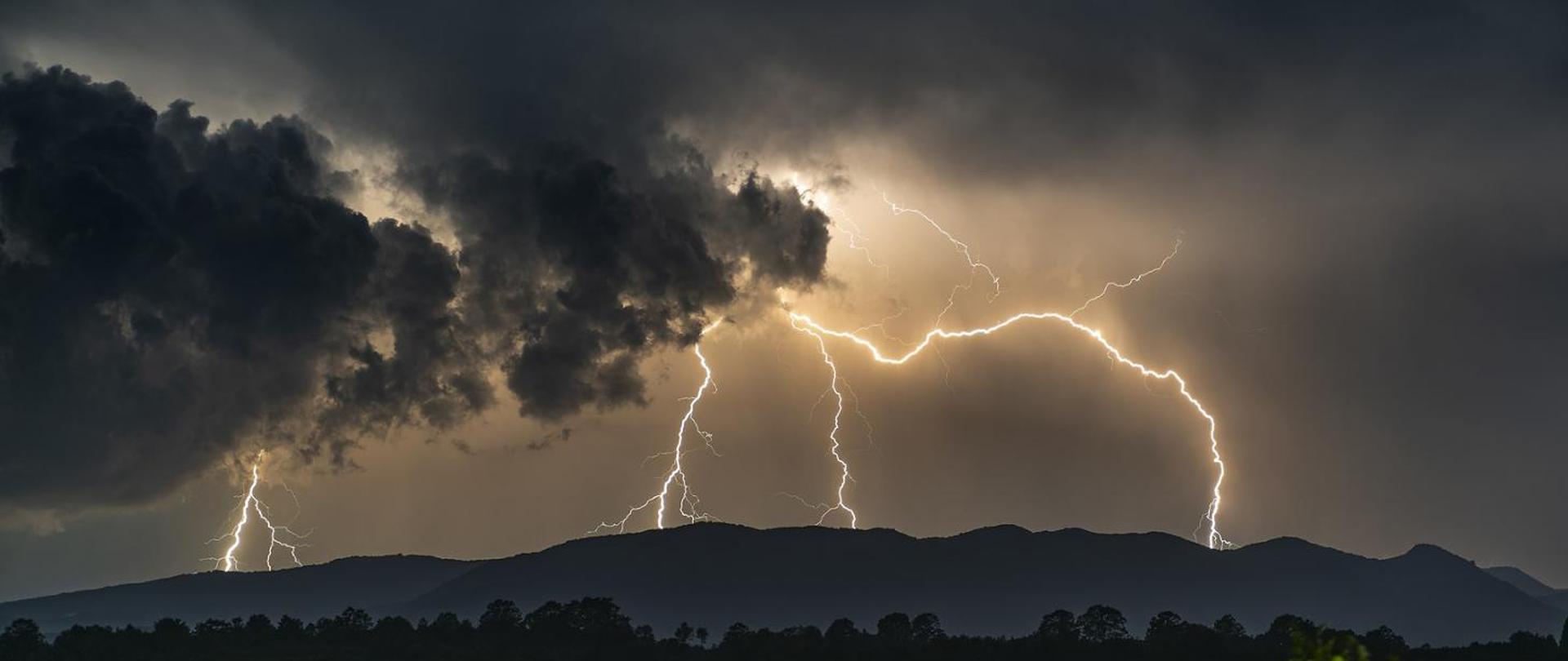 Zdjęcie przedstawia ciemne chmury oraz kilkanaście rozświetlających niebo piorunów.