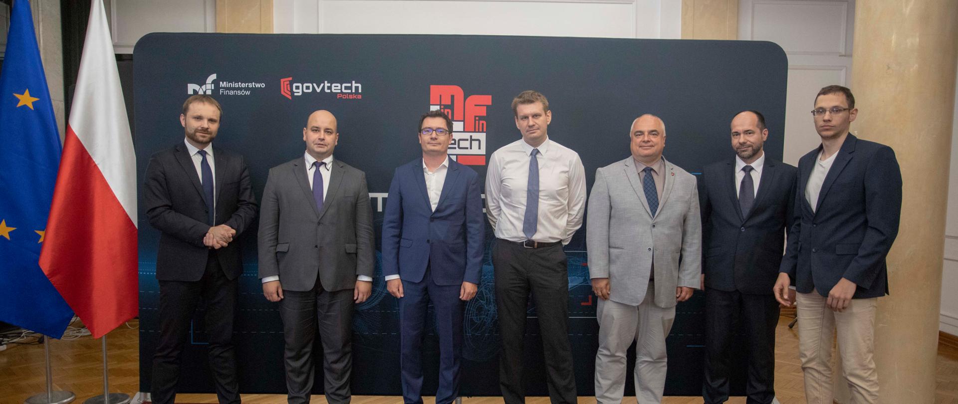 Minister Tomasz Słaboszowski wraz ze współpracownikami na tle banera MF i GOV TECH