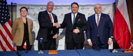 Na środku szefowie NuScale i KGHM podają sobie ręce trzymając w teczka podpisane dokumenty. Po prawej stronie wicepremier Jacek Sasin. W tle flagi Polski i USA