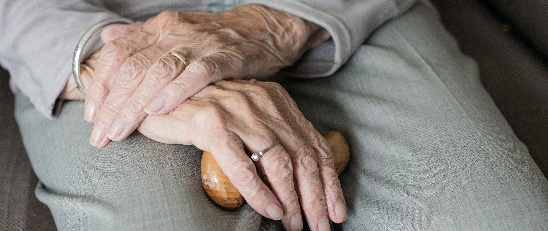 Dłonie oparte o laskę, którą trzyma kobieta w starszym wieku 