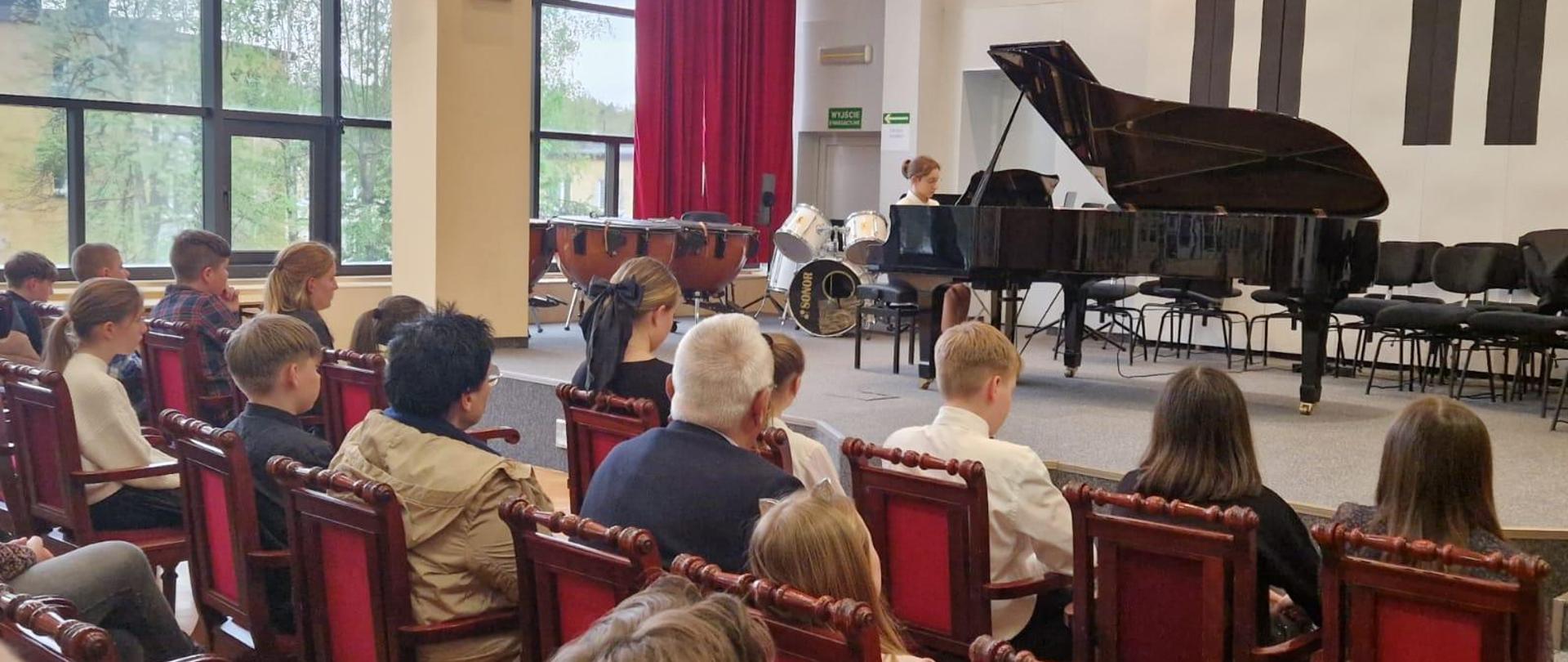 Dziewczynka gra na fortepianie, z przodu widoczna publiczność