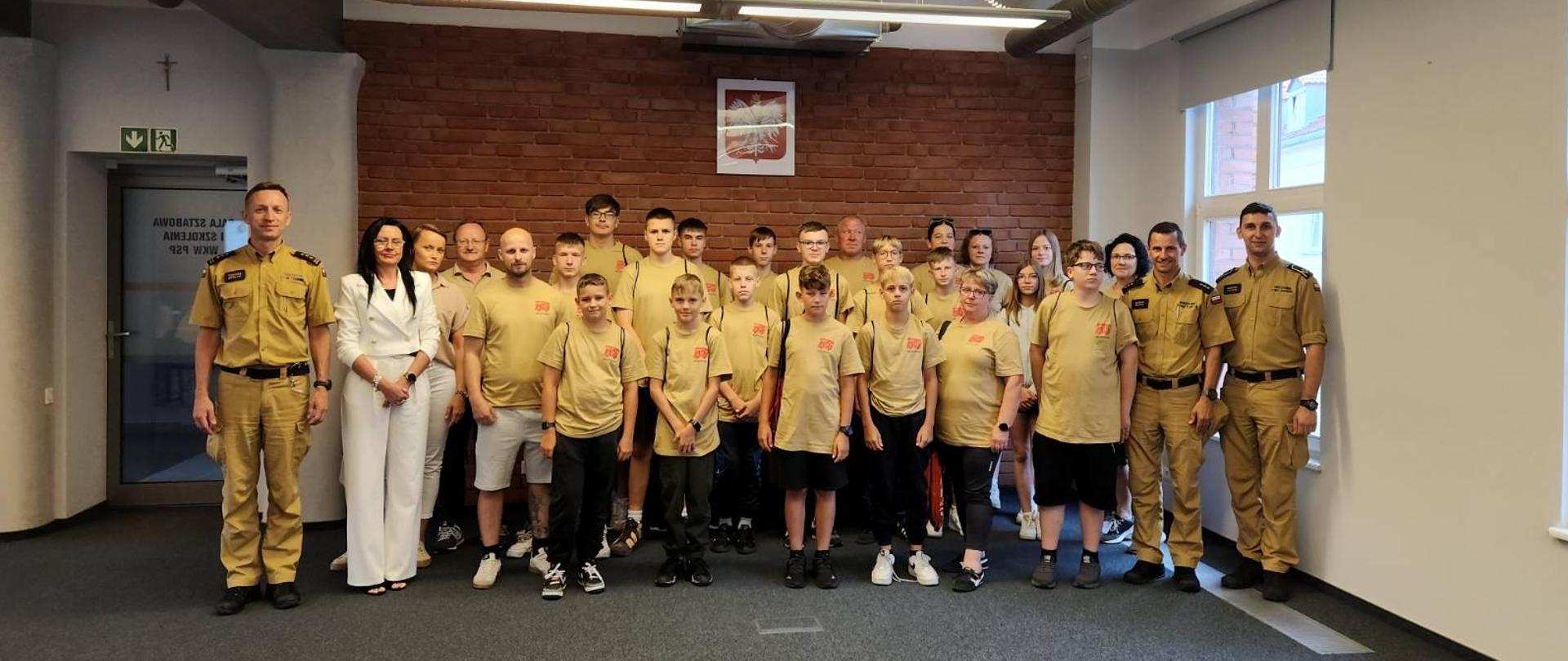 Na zdjęciu znajduje się cała grupa obozowiczów z opiekunami i Panami Komendantami ustawiona do zdjęcia grupowego na sali sztabowej poznańskiej komendy wojewódzkiej PSP.