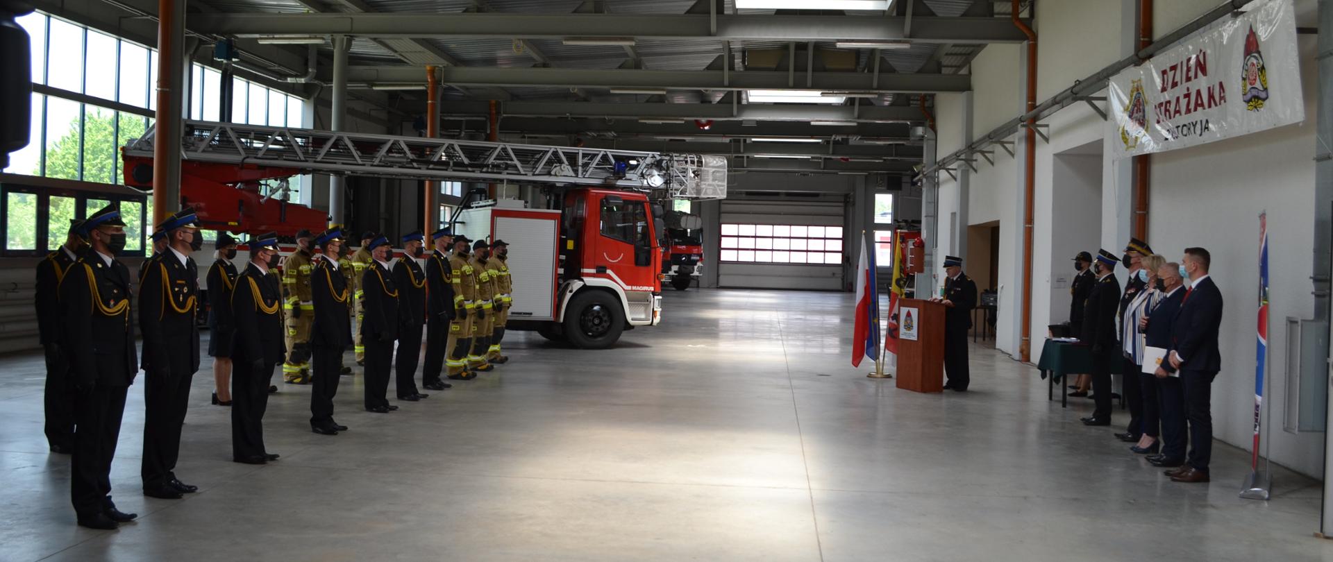 stojący w szyku umundurowani strażacy w garażu JRG, po prawej stronie zaproszeni goście