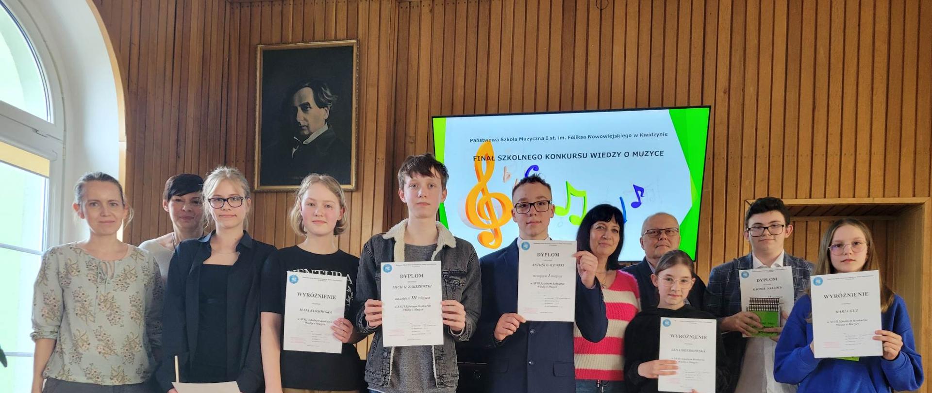 Fotografia przedstawiająca nauczyciela i uczniów trzymających dyplomy konkursowe