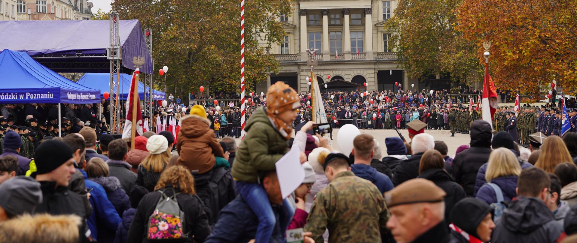 Tłum ludzi z bało czerwonymi balonami i flagami, z lewej strony niebieskie namioty,