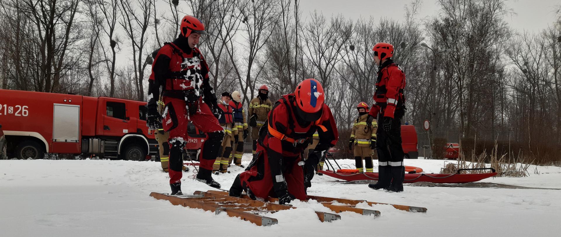 Zdjęcie przedstawia grupę strażaków przygotowujących się do ćwiczeń z zakresu ratownictwa lodowego.
