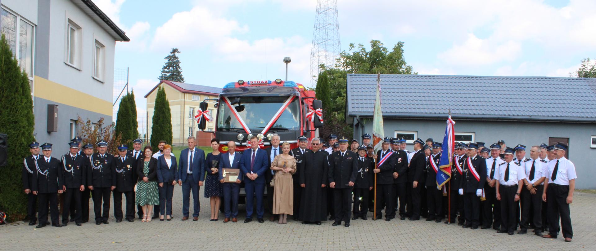 Zaproszeni goście oraz strażacy-ochotnicy na tle samochodu ratowniczo-gaśniczy na podwoziu VOLVO pozyskanego przez OSP Topczewo podczas uroczystości jego wyświęcenia.