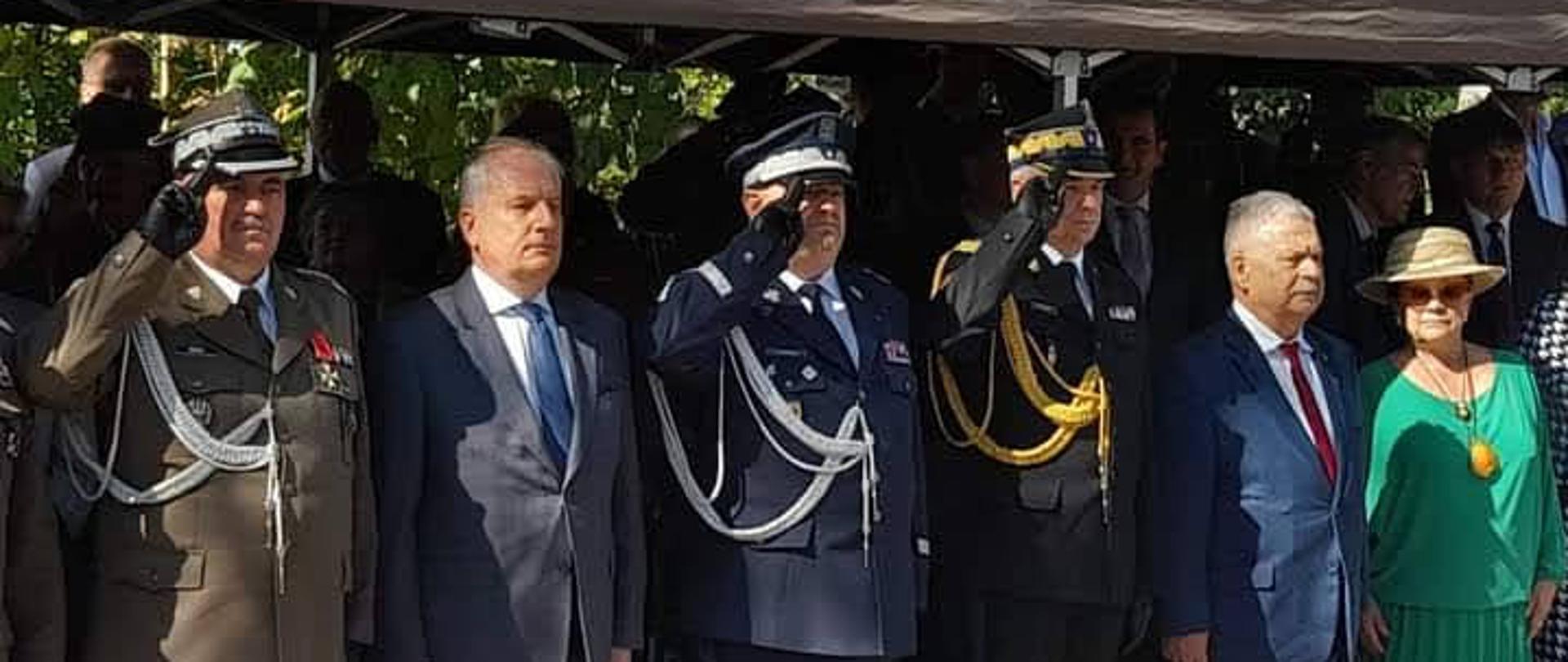 Pomorski komendant wojewódzki Państwowej Straży Pożarnej wspólnie z zaproszonymi gośćmi oddaje honor stojąc w rzędzie.