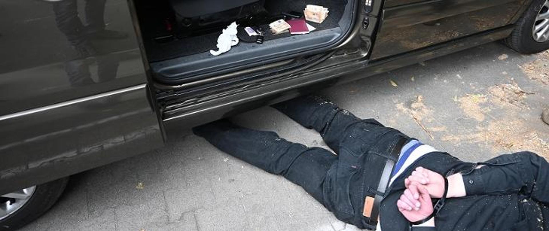 mężczyzna skuty kajdankami leżący przed samochodem