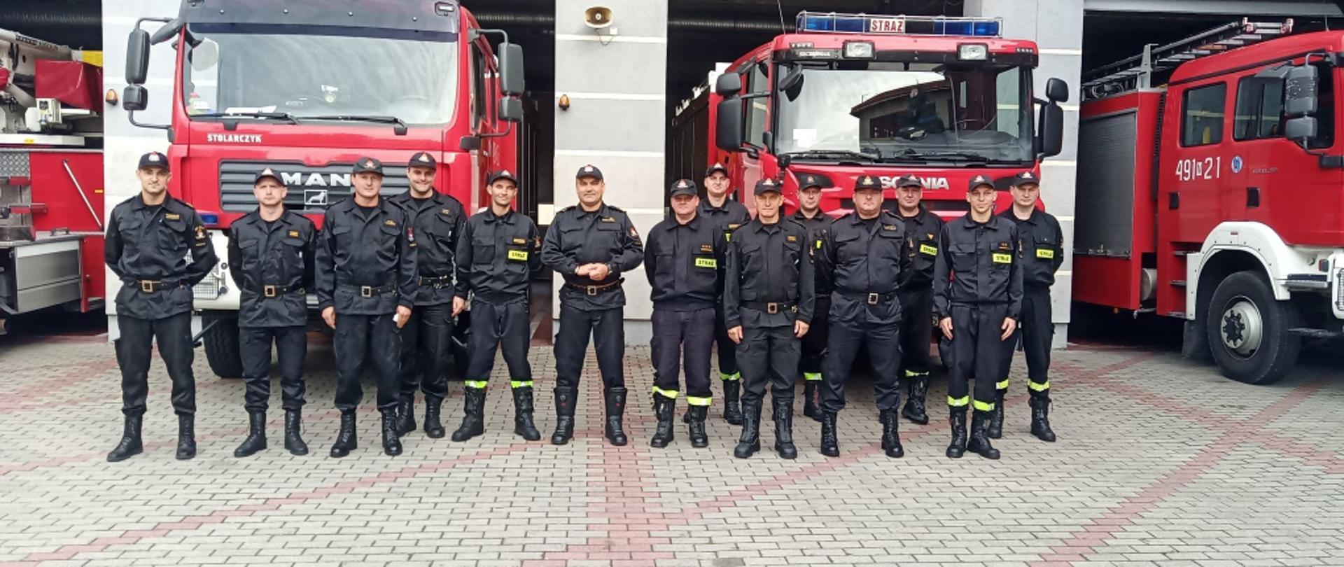 zdjęcie strażaków z KM PSP w Mrągowie na tle pojazdów ratowniczo-gaśniczych