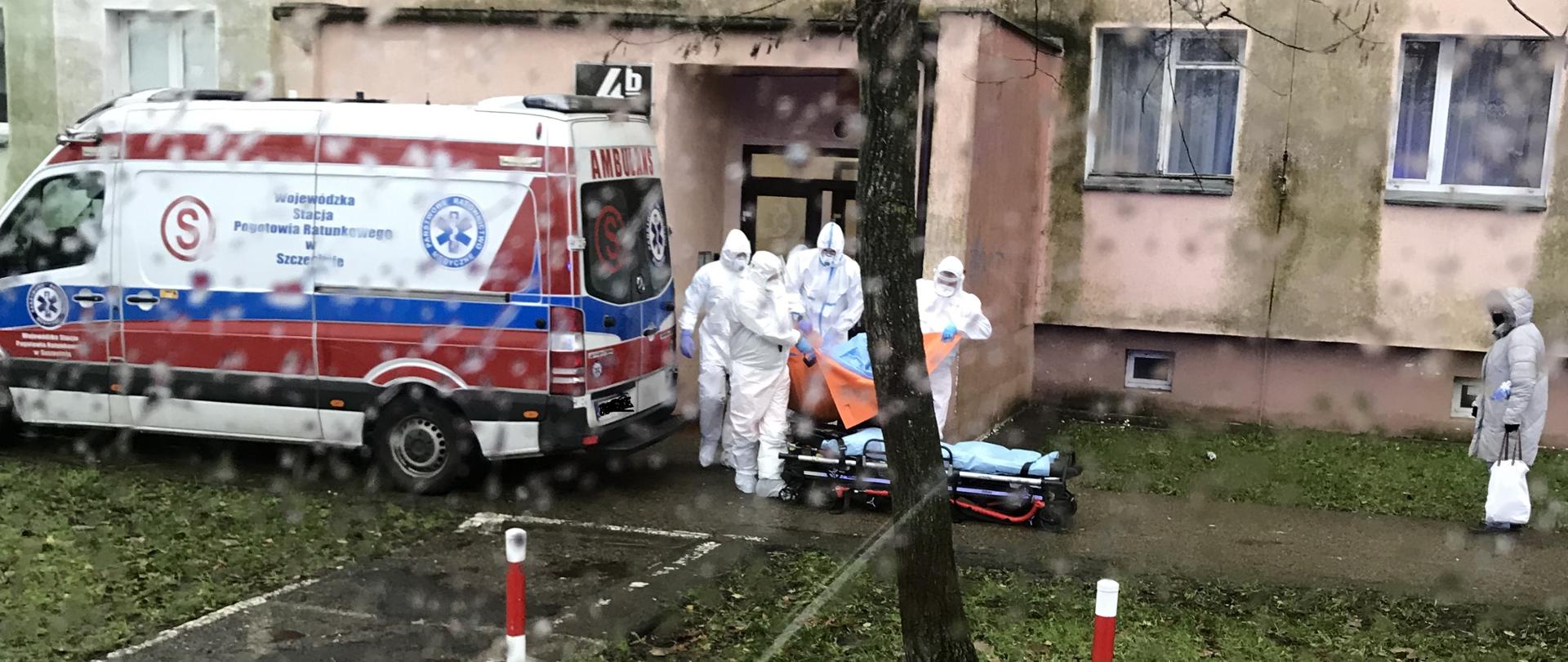 Pomoc PRM w zniesieniu pacjenta z COVID-19. Strażacy w specjalnych ubraniach ochronnych.
