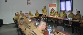 Grupa strażaków na sali konferencyjnej, przemawia Zastępca Komendanta Powiatowego PSP