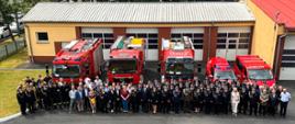 Zdjęcie grupowe wszystkich uczestników uroczystości na tle pojazdów pożarniczych JRG Olesno. Na drugim planie widoczne budynki KP PSP w Oleśnie.