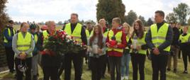Minister Czarnek stoi w otoczeniu grupy młodzieży, w rękach trzyma wieniec biało-czerwonych kwiatów.