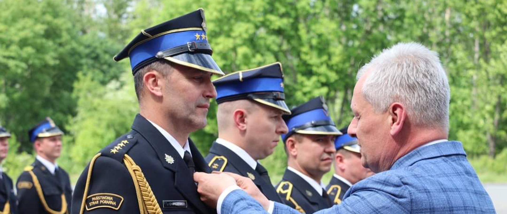 Na zdjęciu znajdują się strażacy wśród nich jeden odznaczany przez osobę cywilną