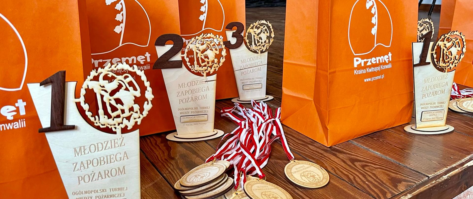 Na stole stoją puchary oraz nagrody, wręczane za udział w turnieju wiedzy pożarniczej.