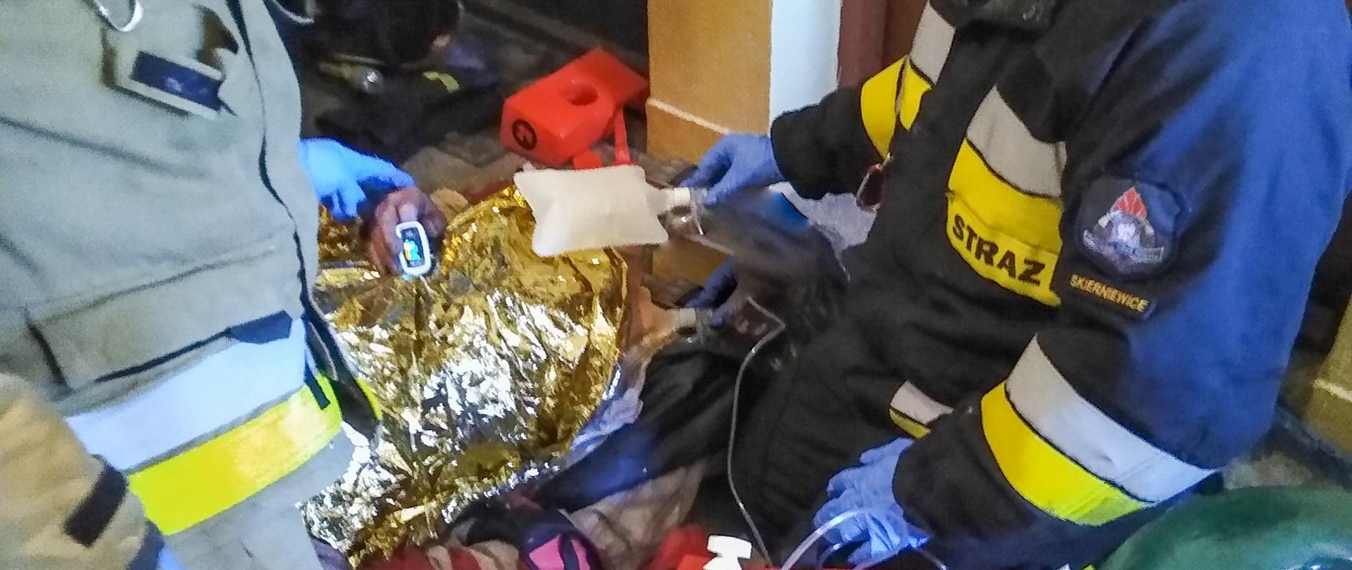 Na zdjęciu widać strażaków udzielających pierwszej pomocy osobie ewakuowanej z mieszkania objętego pożarem.