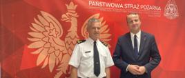 Na zdjęciu widoczny Wojewoda Wielkopolski Pan Michał Zieliński (po prawej) stoi wraz z Komendantem Powiatowym PSP w Wolsztynie bryg. Romanem Rembielakiem. W tle baner w kolorze czerwonym z symbolem orła oraz napisem Państwowa Straż Pożarna.