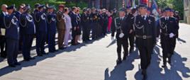 Widok z przodu. Uroczysta defilada. Po lewej stronie goście, mundurowi salutują. Po prawej stronie pododdział pocztów sztandarowych prowadzonych przez druha OSP. 