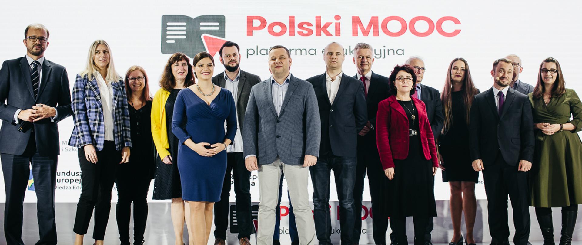 Na zdjęciu widać uczestników wydarzenia, którzy stoją na scenie - m.in. ministra Piotra Dardzińskiego. Na scenie wyświetla się napis: Polski MOOC.