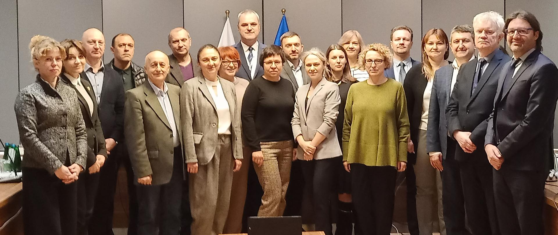 W sali konferencyjnej do zdjęcia pozuje grupa kobiet i mężczyzn 