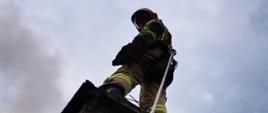 Strażak gasi pożar sadzy w kominie - stoi na kominie zpięty linką