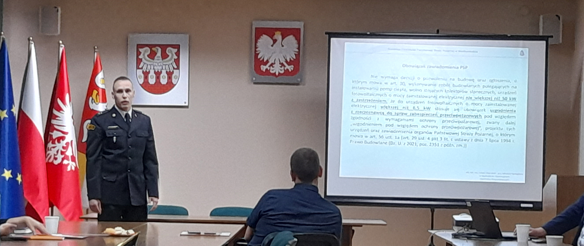 Na zdjęciu widać funkcjonariusza KP PSP w Międzychodzie podczas konferencji oraz uczestników. W tle widać salę na której odbyła się konferencja.
