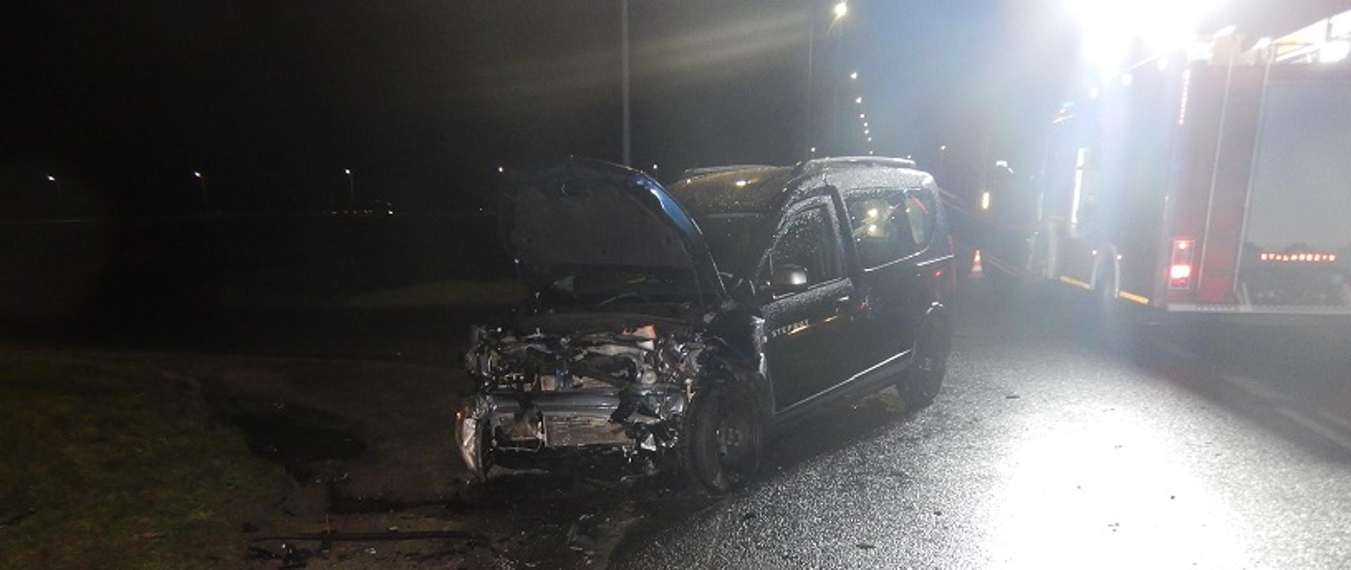 Wypadek w miejscowości Police Średnie gm. Kościelec. Zdjęcie przedstawia przód uszkodzonego samochodu w porze nocnej oraz stojący obok pojazd pożarniczy, który oświetla teren prowadzonych działań