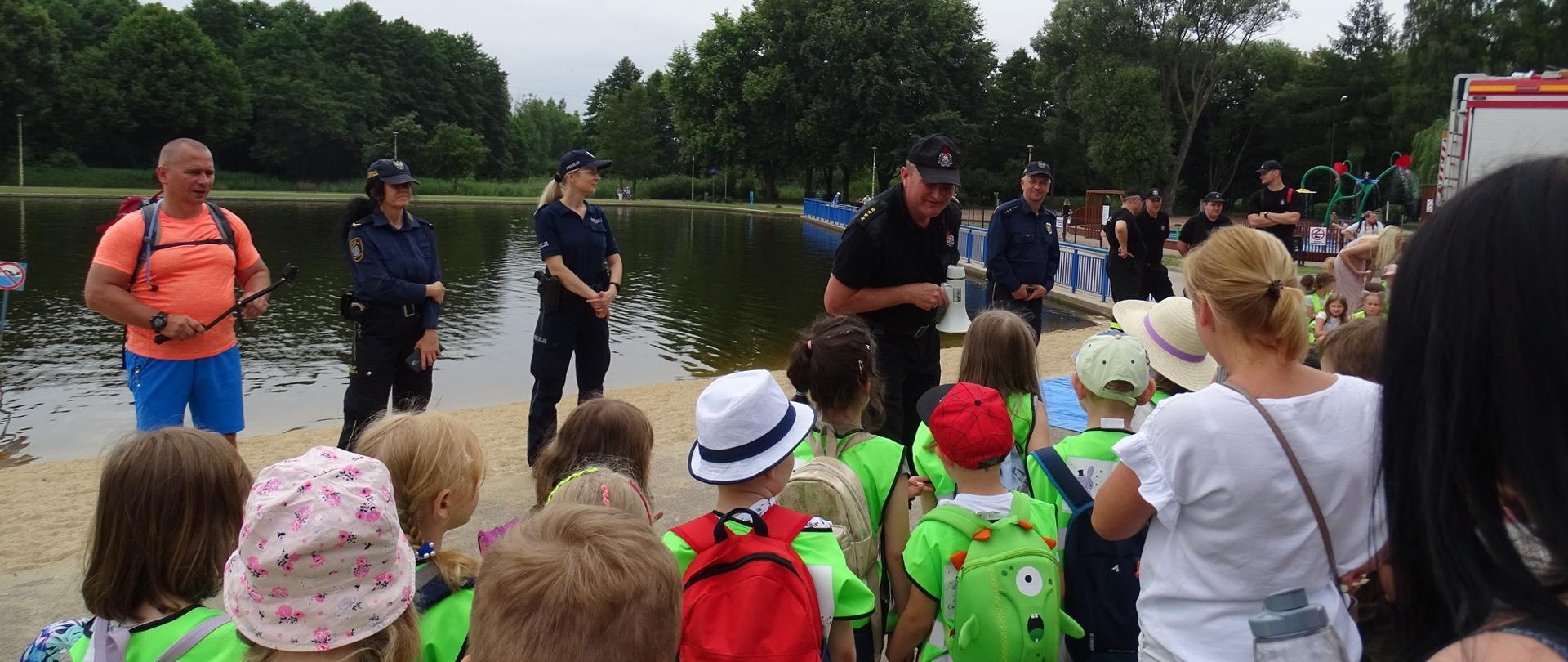 Zdjęcie przedstawia grupę dzieci uczestniczących w pogadance w ramach akcji "Bezpiecznie nad wodą" współorganizowanej przez Państwową Straż Pożarną. 