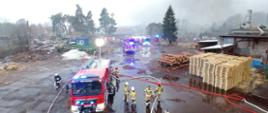 Zdjęcie przedstawia samochody pożarnicze i strażaków na tle pożaru tartaku w Tucznie 
