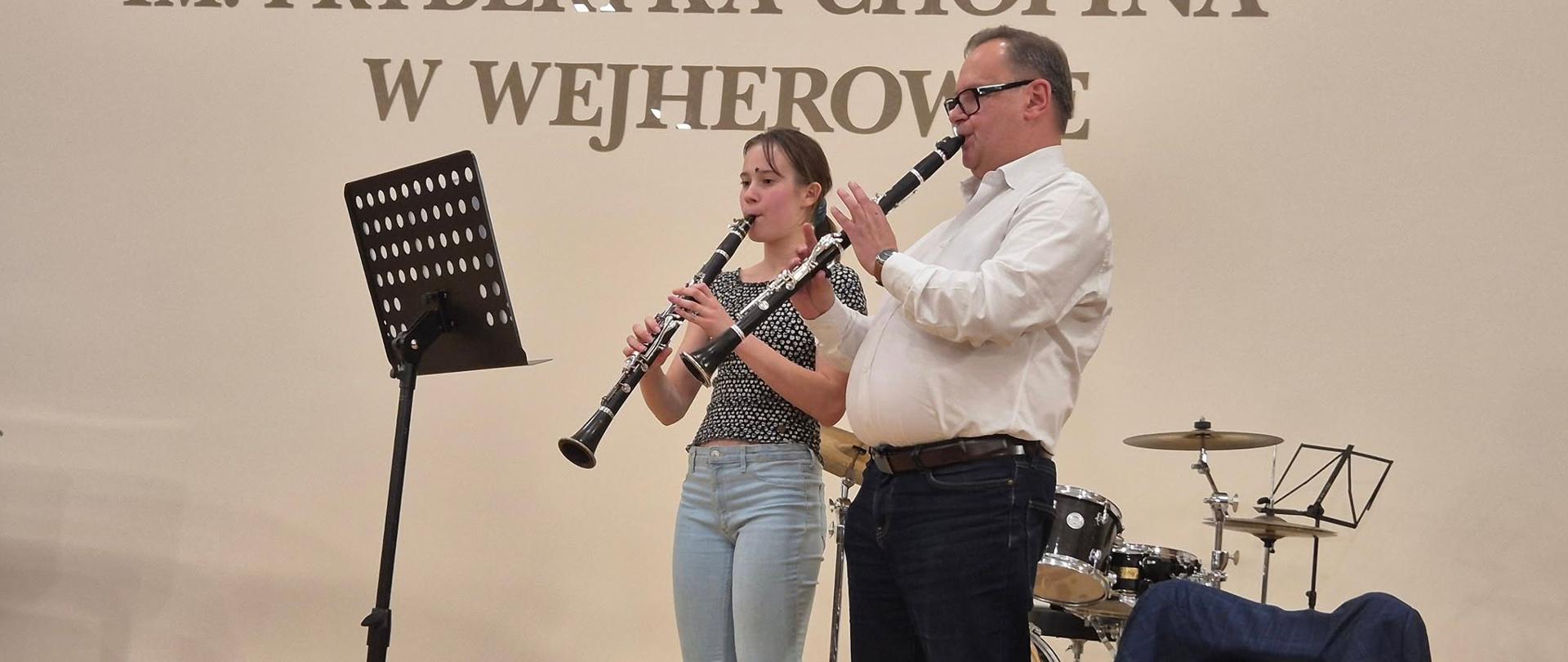 Prof. Grzegorz Wieczorek wraz z uczennicą klasy klarnetu grają na stojąco podczas spotkania metodycznego.