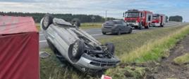 Zdjęcie przedstawia pojazd Audi w pozycji na dachu oraz przyczepkę samochodową w pozycji na boku leżące na poboczu DK nr 78. W tle widać pojazdy pożarnicze