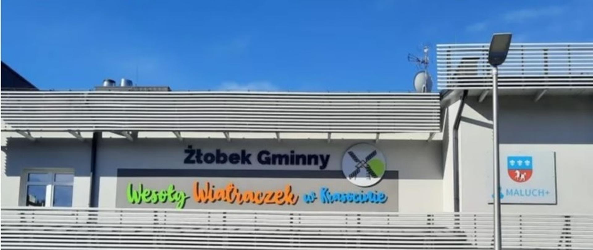 Elewacja frontowa budynku żłobka, w górnej części elewacji szyld Żłobek Gminny „Wesoły Wiatraczek” oraz herb Gminy Krasocin