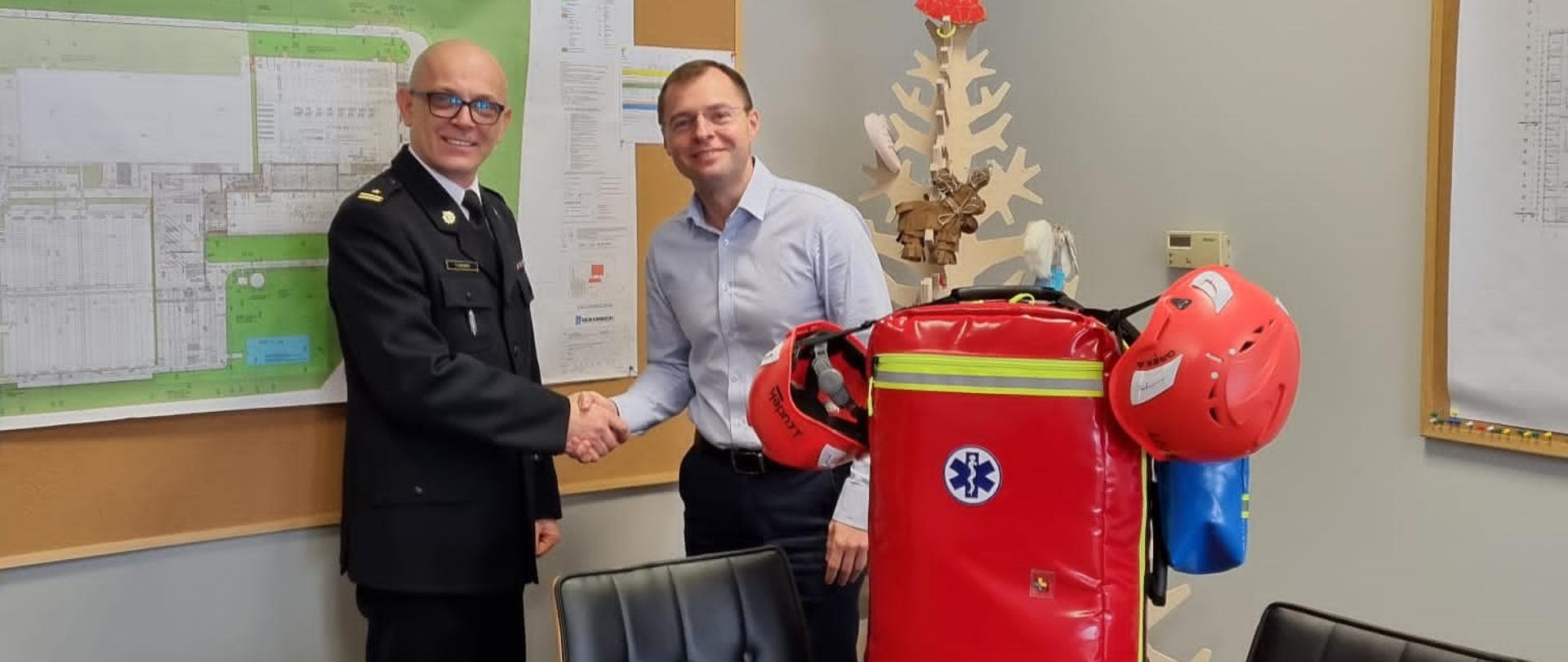 Na zdjęciu komendant powiatowy PSP w Śremie z Prezesem firmy LEOPOL podczas przekazania torby ratownika medycznego która ustawiona jest na stole 