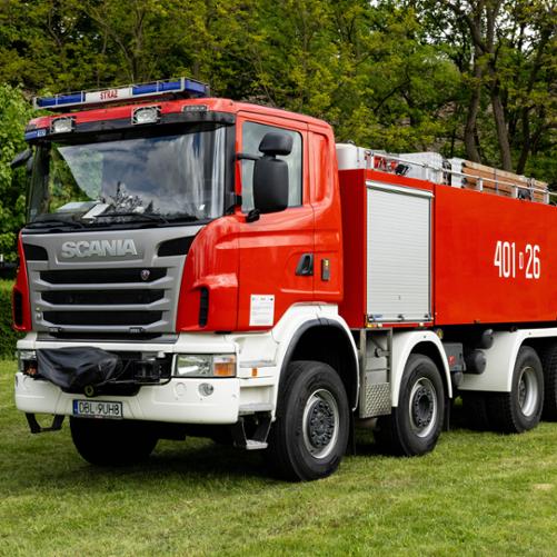 Ciężki, czteroosiowy samochód gaśniczy Scania G480 w charakterystycznym czerwonym kolorze z białymi błotnikami. Na dużym, gładkim boku zabudowy umieszczono biały numer operacyjny „401[D]26”. Na dachu widoczna jest m.in. drabina pożarnicza.