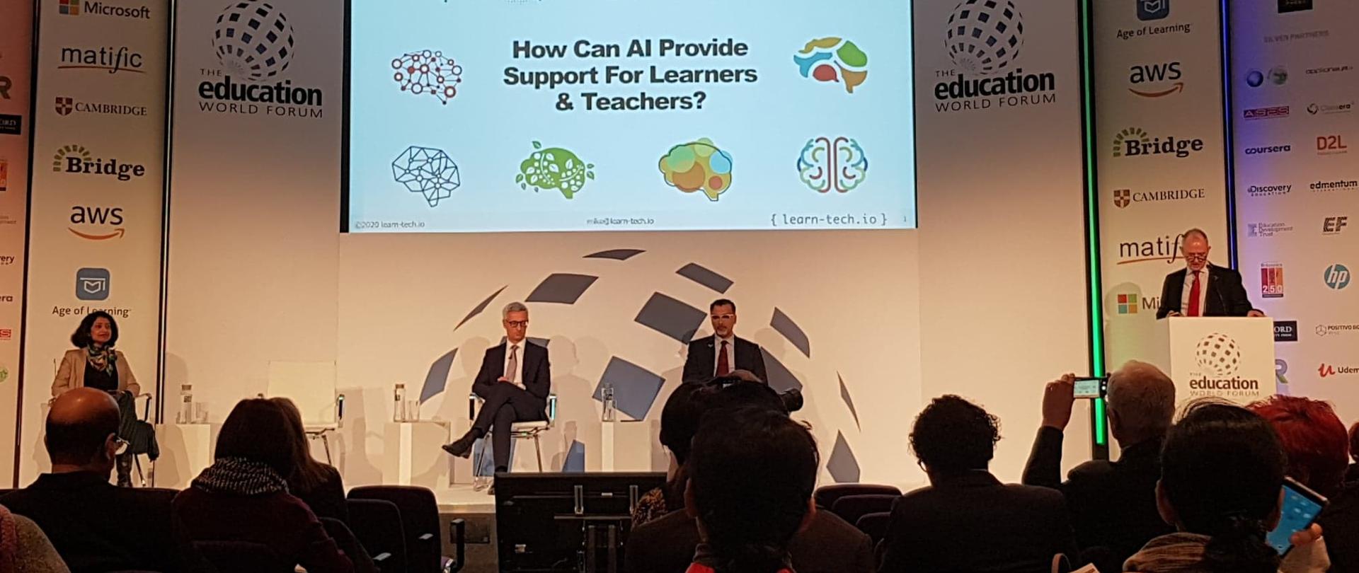 Uczestnicy forum siedzą przed widownią. W tle białe ścianki z różnymi logotypami.