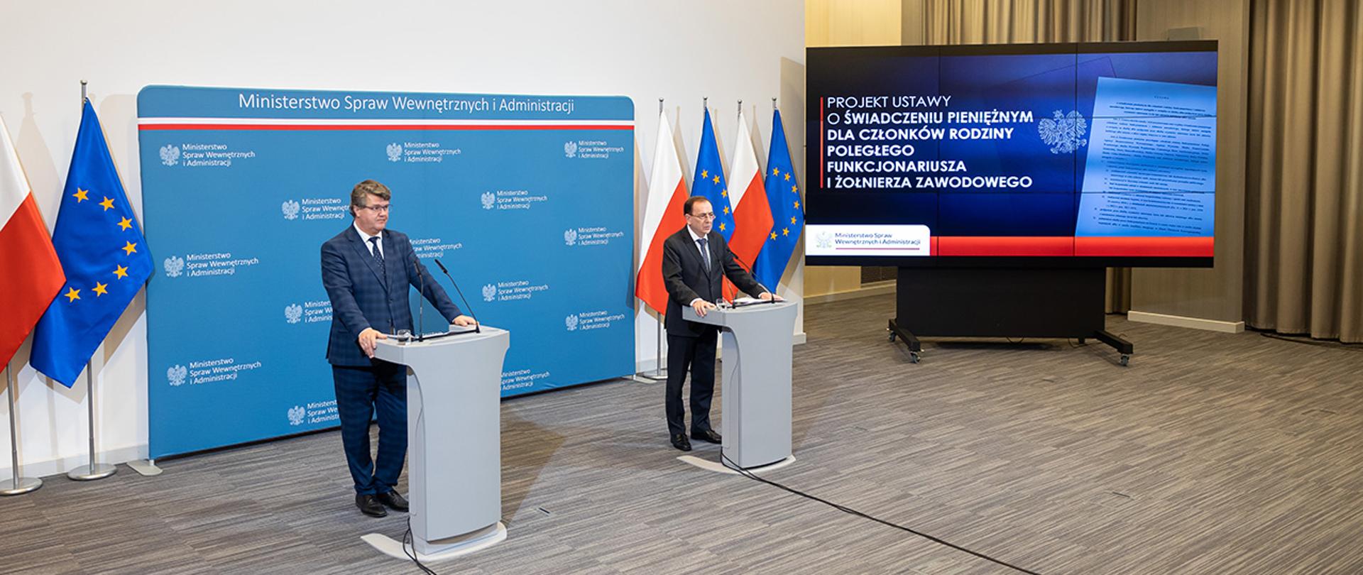 Na zdjęciu widać ministra Mariusza Kamińskiego i wiceministra Macieja Wąsika w trakcie konferencji prasowej stojących za mównicami. 