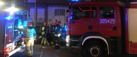 Widoczne dwa samochody pożarnicze przy akcji i strażacy, którzy rozwijają linie gaśnicze.