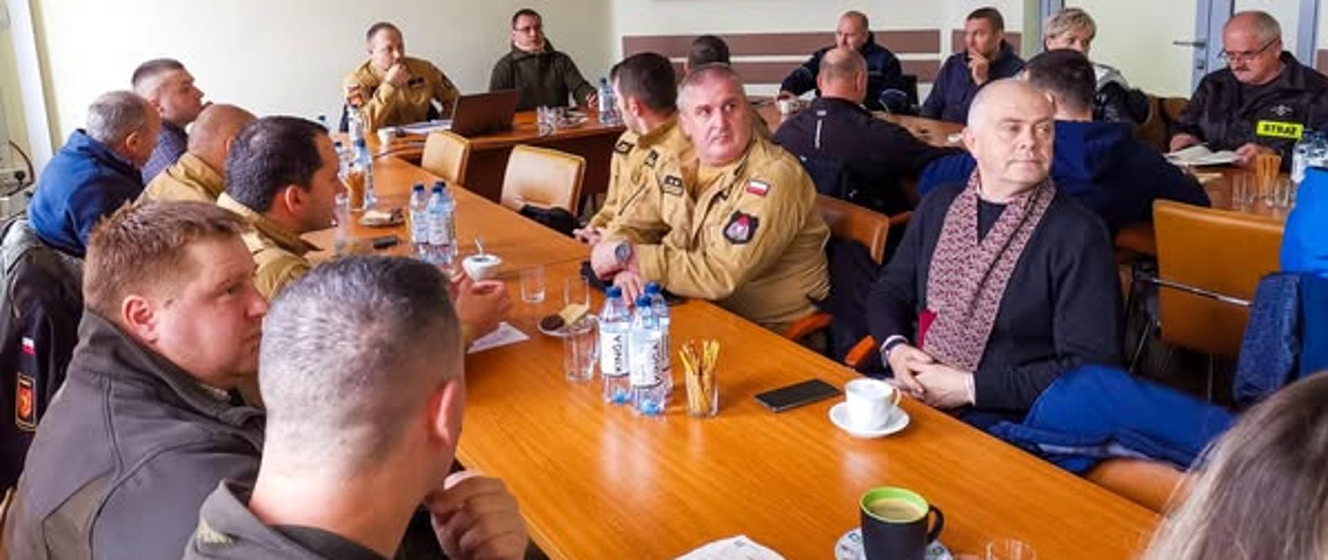 Na zdjęciu widać przedstawicieli Nadleśnictwa, Państwowej Straży Pożarnej oraz Ochotniczej Straży Pożarnej. Wszystkie osoby siedzą przy stołach. Spotkanie dotyczy zbliżających się ćwiczeń "Bieszczady 2024".
