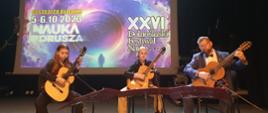 Zdjęcie przedstawia trio gitarzystów podczas trwającego Dolnośląskiego Festiwalu nauki w Bystrzycy Kłodzkiej w auli Miejskiego Ośrodka kultury w Bystrzycy Kłodzkiej. 