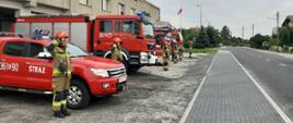 Zdjęcie przedstawia funkcjonariuszy Jednostki Ratowniczo - Gaśniczej w Krośnie Odrzańskim pomiędzy pojazdami pożarniczymi podczas oddawania hołdu Powstańcom na tle bram garażowych jednostki.