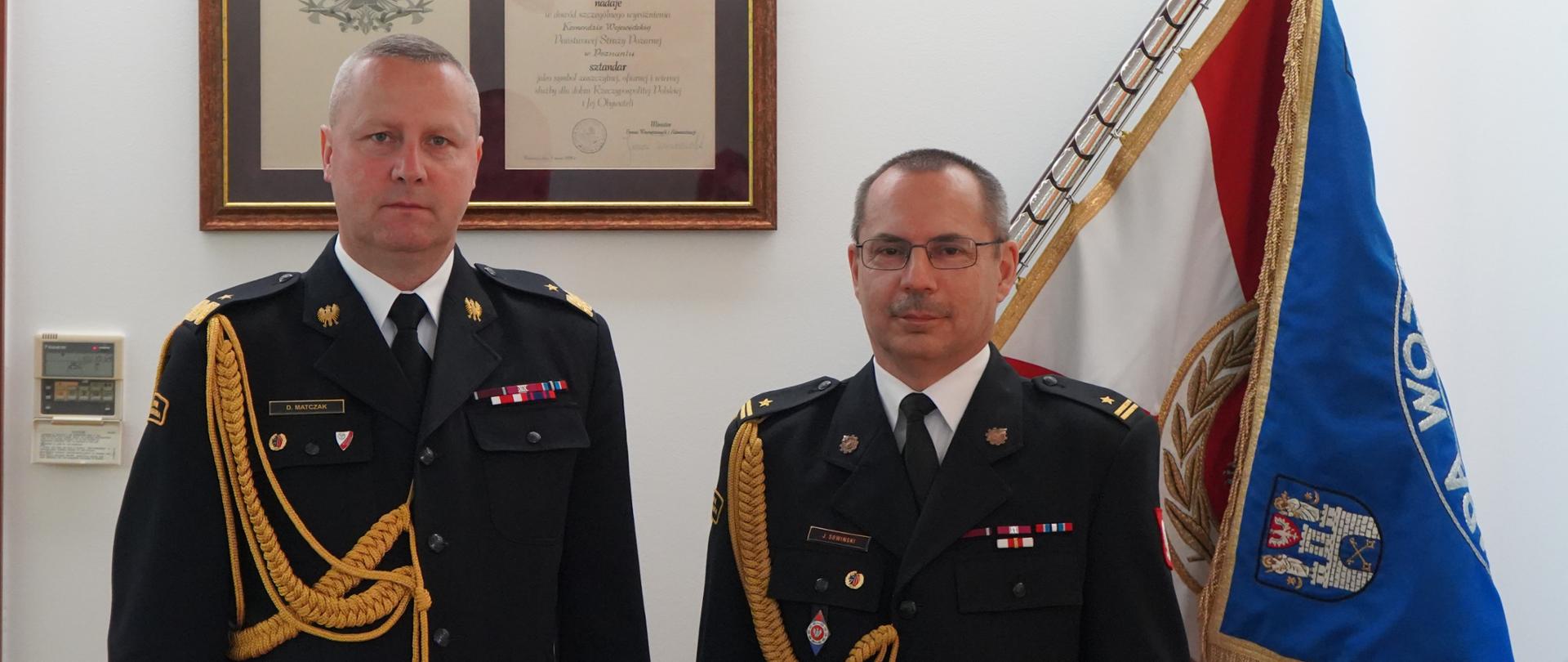 Zdjęcie przedstawia dwóch strażaków którzy stoją obok siebie i pozują do zdjęcia. Ubrani są w mundury służbowe. Jeden z nich trzyma w ręce decyzję powierzenia obowiązków Zastępcy Komendanta.
