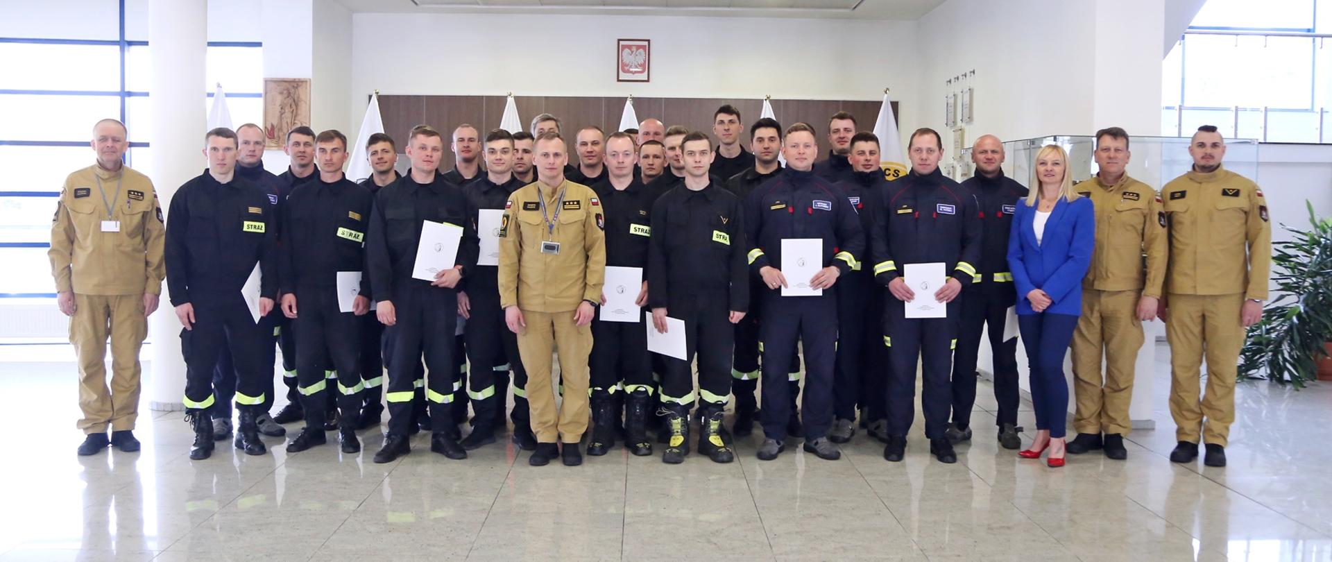 Grupowe zdjęcie uczestników szkolenia (26 osób) w towarzystwie Zastępcy Komendanta Centralnej Szkoły PSP, kobiety oraz trzech funkcjonariuszy CS PSP