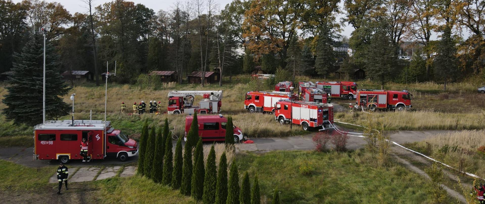 czerwone samochody z oznaczeniami strażackimi stoją na zielonej trawie 